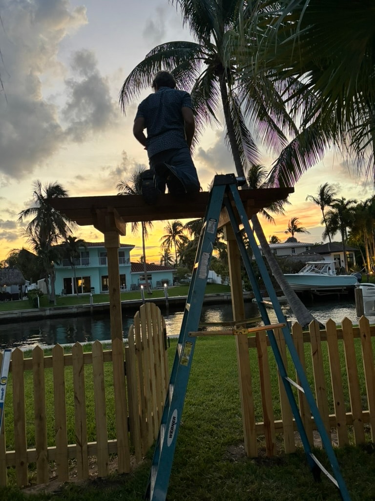 Worker on ladder installing trellis at sunset by waterfront
